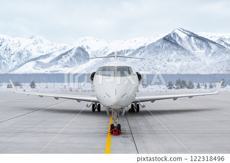 Front view of the modern white corporate airplane at the airport apron on the background of high scenic snow capped mountains 122318496