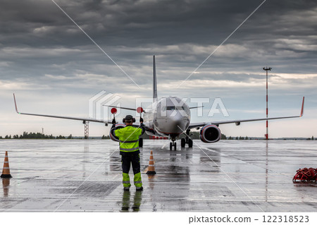 Airliner marshalling at the aiport apron in rainy weather. Passenger jet plane meeting 122318523
