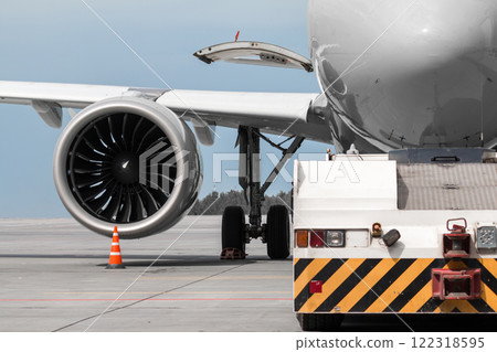 Close-up tow truck near the passenger airplane. Close-up of engine and main landing gear of aircraft Close-up tow truck near the passenger airplane. Close-up of engine and main landing gear of aircraft 122318595