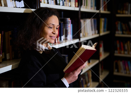 A woman is enjoying a book in a cozy library, surrounded by shelves of books. The scene highlights learning, personal exploration, and the tranquil atmosphere of reading in a library. 122320335
