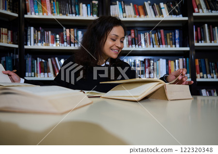 Young woman studying at a library table with open books, surrounded by bookshelves. Capturing the importance of reading, researching, and academic life, evoking the essence of World Book Day or Young woman studying at a library table with open books, surrounded by bookshelves. Capturing the importance of reading, researching, and academic life, evoking the essence of World Book Day or 122320348