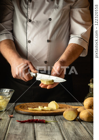 A chef expertly slices a potato with precision in a rustic kitchen, surrounded by fresh produce and tools, highlighting the art of culinary preparation and dedication to quality 122320558