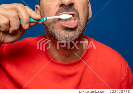 Close up of bearded hispanic man in his 40s brushing his teeth, isolated on blue studio background. Dental hygiene and health concept. Close up of bearded hispanic man in his 40s brushing his teeth, isolated on blue studio background. Dental hygiene and health concept. 122320778