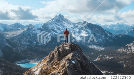 Hiker on Rocky Summit Overlooking Snow-Capped Mountain Peaks and Alpine Lake 122322500