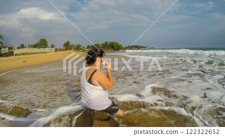 A middle-aged Asian woman sitting on a rock on a sunset beach in Liberia, West Africa. A middle-aged Asian woman sitting on a rock on a sunset beach in Liberia, West Africa. 122322652