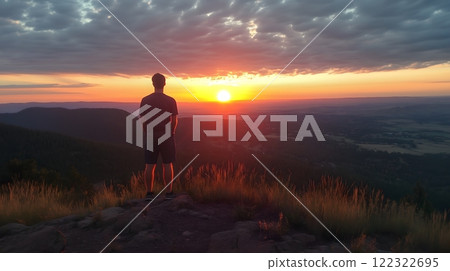 Hiker Standing on a Hilltop Watching a Fiery Sunrise 122322695