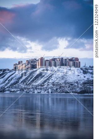 Beautiful view of a residential neighborhood of apartment buildings on a winter evening on the banks of the Yenisei River in Krasnoyarsk, Russia. Snowy Riverbank Cityscape Featuring Striking Modern 122324049