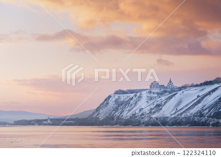 Winter landscape - a Russian Orthodox church snow-covered high bank of the Yenisei River in Krasnoyarsk, Russia. Beautiful view of the Yenisei river at orange sunset 122324110