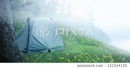 Tent in the fog in the morning behind a green meadow on top of a mountain in a secluded place. 122324120