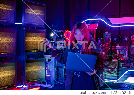 Asian woman in front of a computer monitor display big digital data with laptop computer, neon light, Hacker wear black jacket at system control room, Security guard working on multiple monitors 122325266