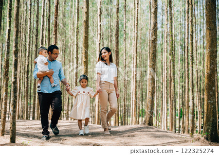 A mother holding her child and father hold baby walking through a field of tall grass in the countryside on a sunny day, Happy family day 122325274