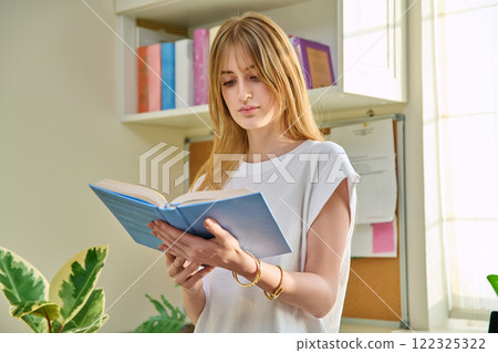 Young teenage female reading book, novel, fiction educational literature at home 122325322