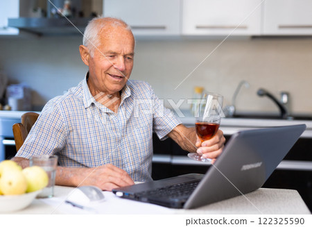 Elderly man with glass of cognac talking through internet Elderly man with glass of cognac talking through internet 122325590