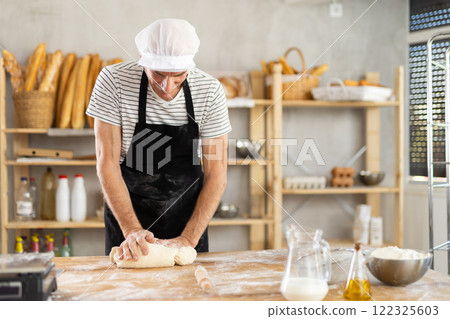 Elderly man kneads dough in bakery 122325603