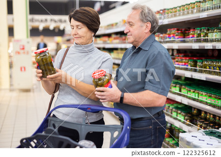 Elderly married couple choosing canned cucumbers together in the grocery section of supermarket Elderly married couple choosing canned cucumbers together in the grocery section of supermarket 122325612