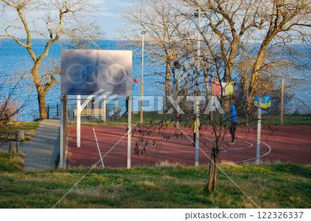 Basketball court with the sea in the background. Behind the advertising board there is a sports board with a ring from which the ball bounced after being thrown. Basketball court with the sea in the background. Behind the advertising board there is a sports board with a ring from which the ball bounced after being thrown. 122326337