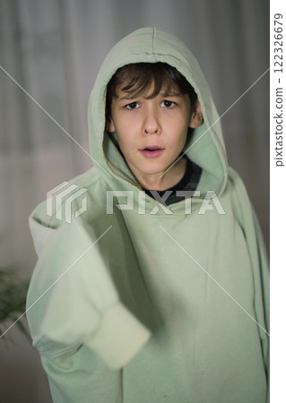 A young boy in a hooded sweatshirt with an expressive gaze, pointing forward with curiosity and engagement. A young boy in a hooded sweatshirt with an expressive gaze, pointing forward with curiosity and engagement. 122326679