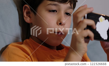child in an orange shirt reacts with delight while using his smartphone, showcasing the thrill and curiosity often sparked by technology in the modern era. 122326688