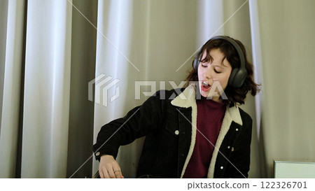 A girl wearing headphones operates a sound mixer with an expressive and joyful attitude. The scene conveys themes of music production, self-expression, and youthful energy. A girl wearing headphones operates a sound mixer with an expressive and joyful attitude. The scene conveys themes of music production, self-expression, and youthful energy. 122326701