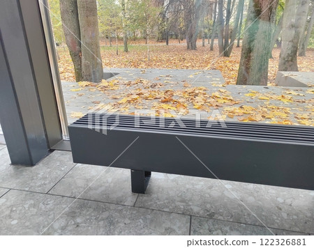 A sleek heating unit by a glass wall, with a tranquil park scene in the background featuring autumn foliage. A balance of modern functionality and nature. A sleek heating unit by a glass wall, with a tranquil park scene in the background featuring autumn foliage. A balance of modern functionality and nature. 122326881