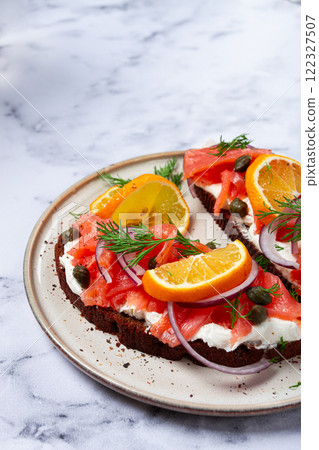 sandwich with freshly smoked salmon, on black bread, with cottage cheese, with herbs and red onions, capers and pieces of citrus fruits, on a marble countertop, breakfast, no people, 122327507