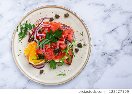 sandwich with freshly smoked salmon, on black bread, with cottage cheese, with herbs and red onions, capers and pieces of citrus fruits, on a marble countertop, breakfast, no people, 122327509