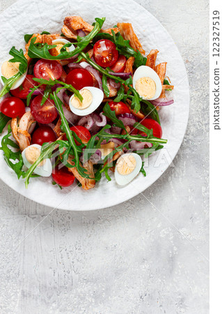 a warm salad with fried chicken fillet, arugula and cherry tomatoes, and boiled quail eggs, on a white plate, no people. 122327519
