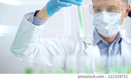 Scientist with protective gloves and glasses examining lab tube with a green fluid. Microbiology and science concept 122329751