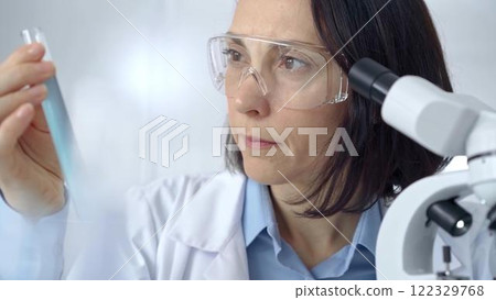 Female scientist analyzing sample in laboratory. Focused female researcher examines a clear test tube in a modern lab setting 122329768