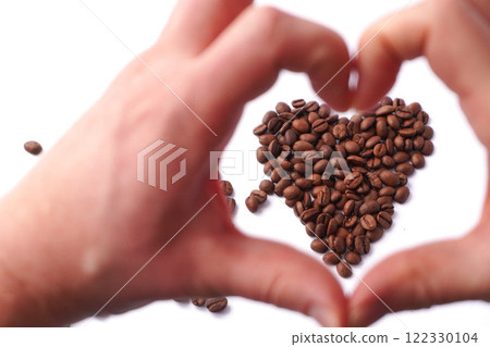 A pair of hands forming a heart shape in the foreground, framing a heart-shaped arrangement of roasted coffee beans on a white background, symbolizing passion, love and appreciation for coffee culture 122330104