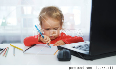 Baby girl at her desk, writing or drawing with a blue pen, with a laptop nearby. Creative freelance work or early development Baby girl at her desk, writing or drawing with a blue pen, with a laptop nearby. Creative freelance work or early development 122330411