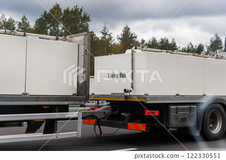 Truck carrying live fish big white tanks highway with forest background. Semi trailer cargo vehicle motorway transporting living aquaculture in large containers. Safe seafood logistics fresh supply 122330551