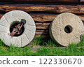 Millstones against the wall of an old wooden house. 122330670