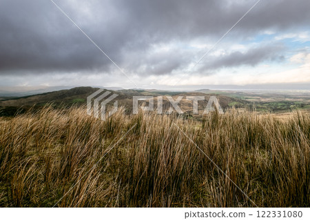 Lush hills stretch across the landscape, covered in tall grass. Dark clouds loom overhead, hinting at an impending change in weather during the afternoon. Lush hills stretch across the landscape, covered in tall grass. Dark clouds loom overhead, hinting at an impending change in weather during the afternoon. 122331080