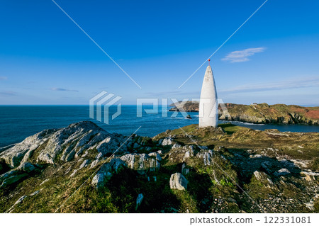Coastal tower. A white, conical tower sits on a rocky, grassy headland, overlooking the sea. The day is bright and sunny. Coastal tower. A white, conical tower sits on a rocky, grassy headland, overlooking the sea. The day is bright and sunny. 122331081