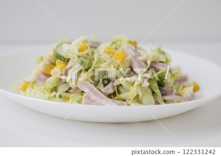 Tasty and healthy salad with cabbage, cucumber, corn, ham and mayonnaise on a white plate. Tasty and healthy salad with cabbage, cucumber, corn, ham and mayonnaise on a white plate. 122331242