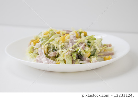 Tasty and healthy salad with cabbage, cucumber, corn, ham and mayonnaise on a white plate. 122331243