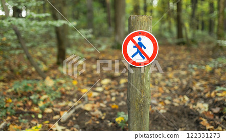 A round sign prohibiting entry into the forest. A no walking sign is posted on a wooden stake on nature background. High quality photo 122331273