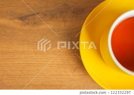 A yellow cup and saucer stands on a wooden background with black tea poured, half of a mug with space for text is visible. The concept of tea drinking, tea tradition, break. High quality photo 122332297