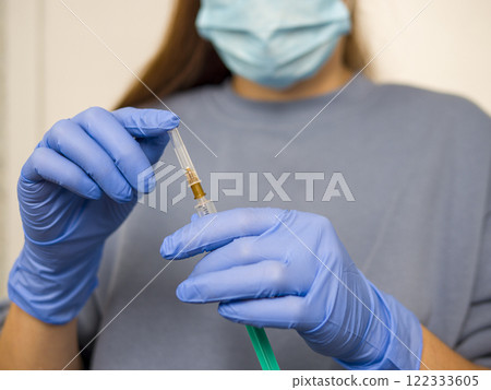 Medical professional wearing protective gear handling vaccine-loaded syringe, preparing immunization procedure with careful precision in clinical setting Medical professional wearing protective gear handling vaccine-loaded syringe, preparing immunization procedure with careful precision in clinical setting 122333605