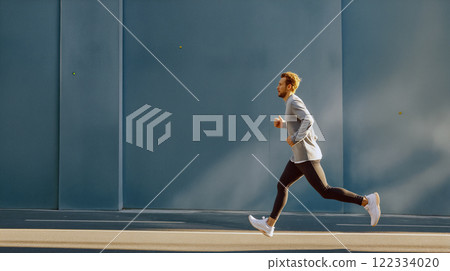 Man running on urban street in modern attire during bright day 122334020