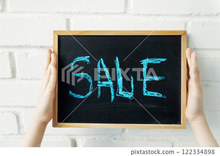 Blue word Sale on black chalk board in children's hands on white brick wall Blue word Sale on black chalk board in children's hands on white brick wall 122334898