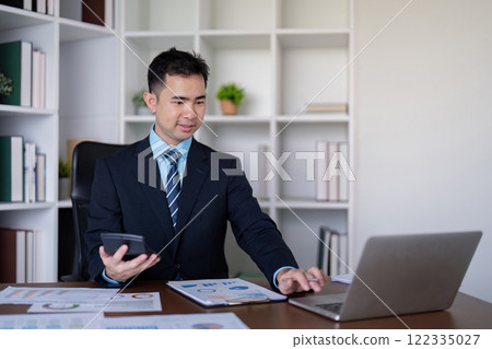 Accountant using a smartphone and laptop to analyze financial data in a modern office 122335027
