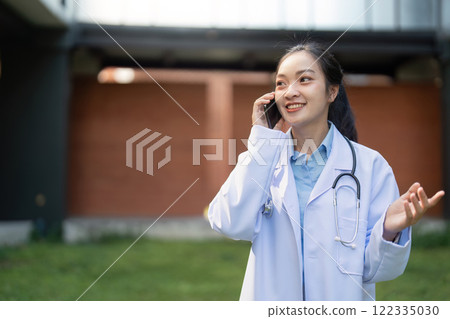 Nurse engaged in a phone conversation, smiling while standing in a contemporary healthcare environment 122335030
