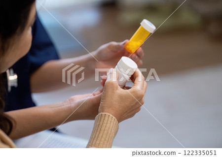 Elderly patient discussing symptoms with caregiver while holding medication bottles Elderly patient discussing symptoms with caregiver while holding medication bottles 122335051