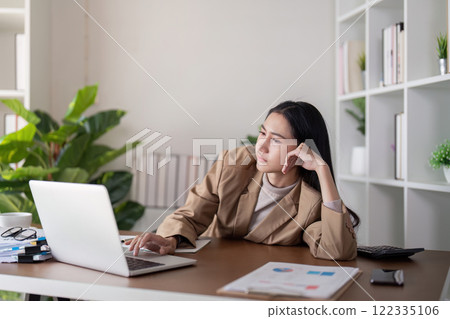 Thoughtful businesswoman deep in concentration while working on a laptop at her modern office desk Thoughtful businesswoman deep in concentration while working on a laptop at her modern office desk 122335106