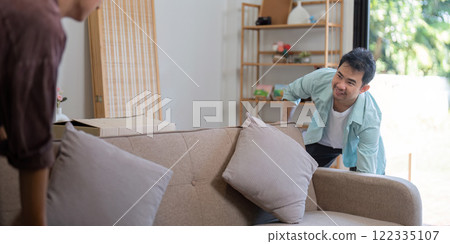 Gay couple arranging their new sofa while smiling in a bright living room Gay couple arranging their new sofa while smiling in a bright living room 122335107