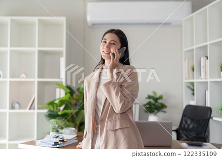 Confident businesswoman smiling while on a phone call in her modern office, showcasing communication skills Confident businesswoman smiling while on a phone call in her modern office, showcasing communication skills 122335109