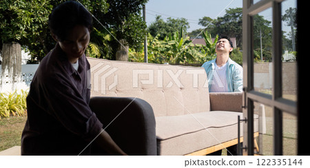 Gay couple moving into a new home, lifting a sofa with laughter in their garden 122335144