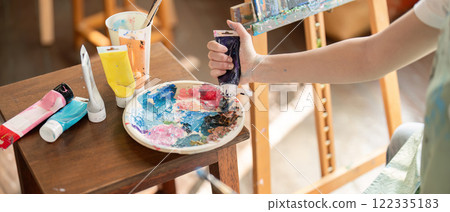 Focused artist squeezing paint tubes onto a palette while preparing to create her next work in a bright studio Focused artist squeezing paint tubes onto a palette while preparing to create her next work in a bright studio 122335183